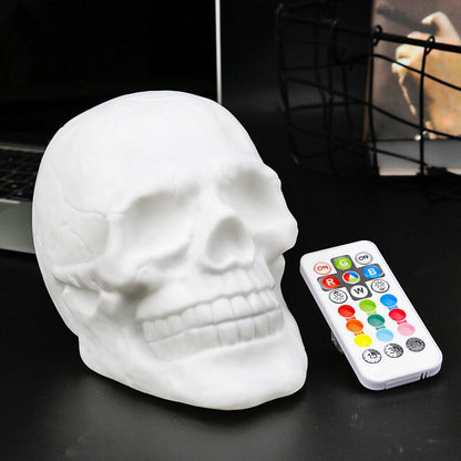 White skull night light switched off on a desk, turned three-quarters, beside its remote control