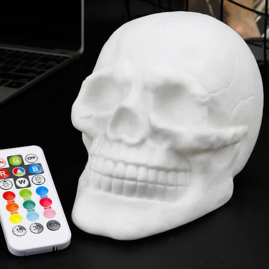 White skull night light switched off, three-quarter view, with its remote control beside it