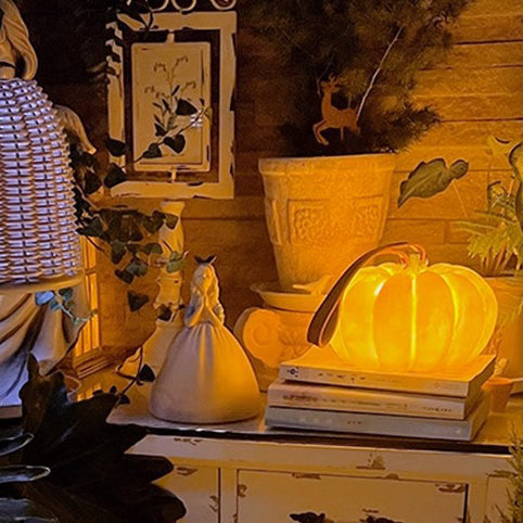 Small solar pumpkin light glowing on a stack of books beside a potted plant
