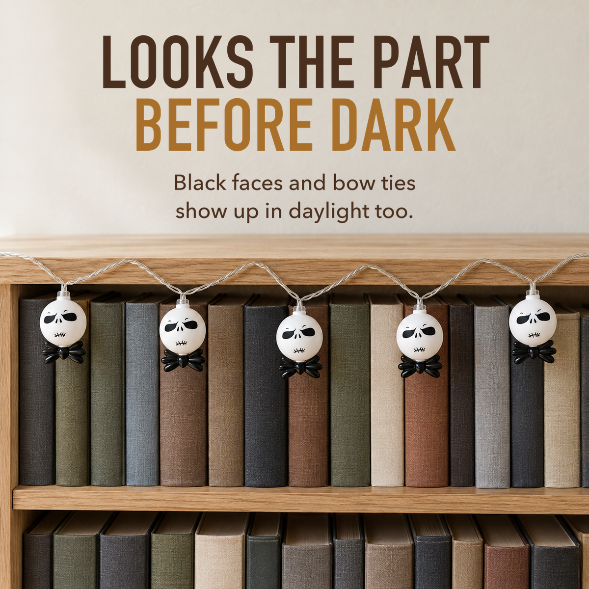 Text image: Looks the part before dark. Unlit white string light heads with black faces and bow ties hanging along a light oak bookcase in daylight