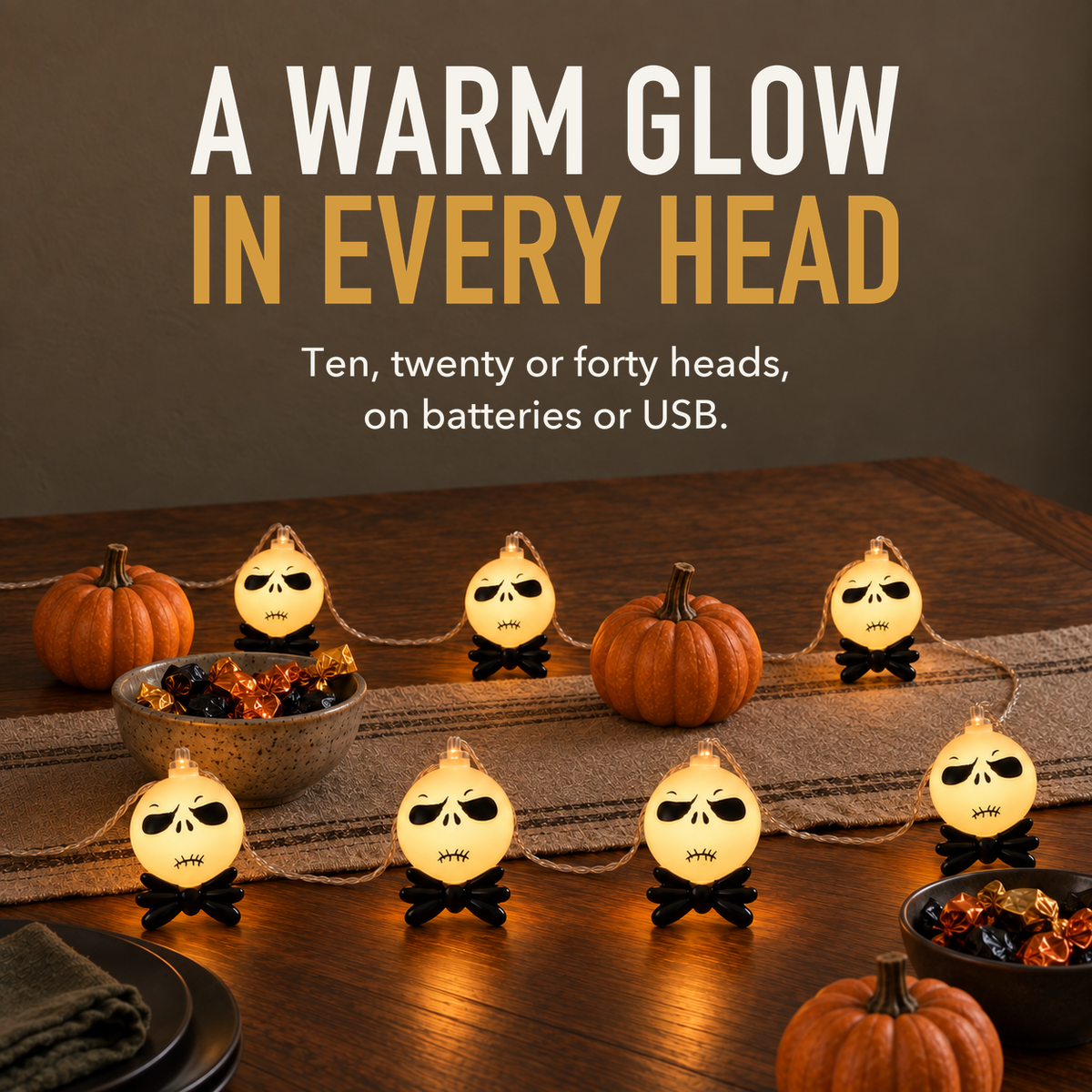 Text image: A warm glow in every head. Lit string light heads standing on their black bow ties along a walnut party table, with bowls of sweets and small pumpkins