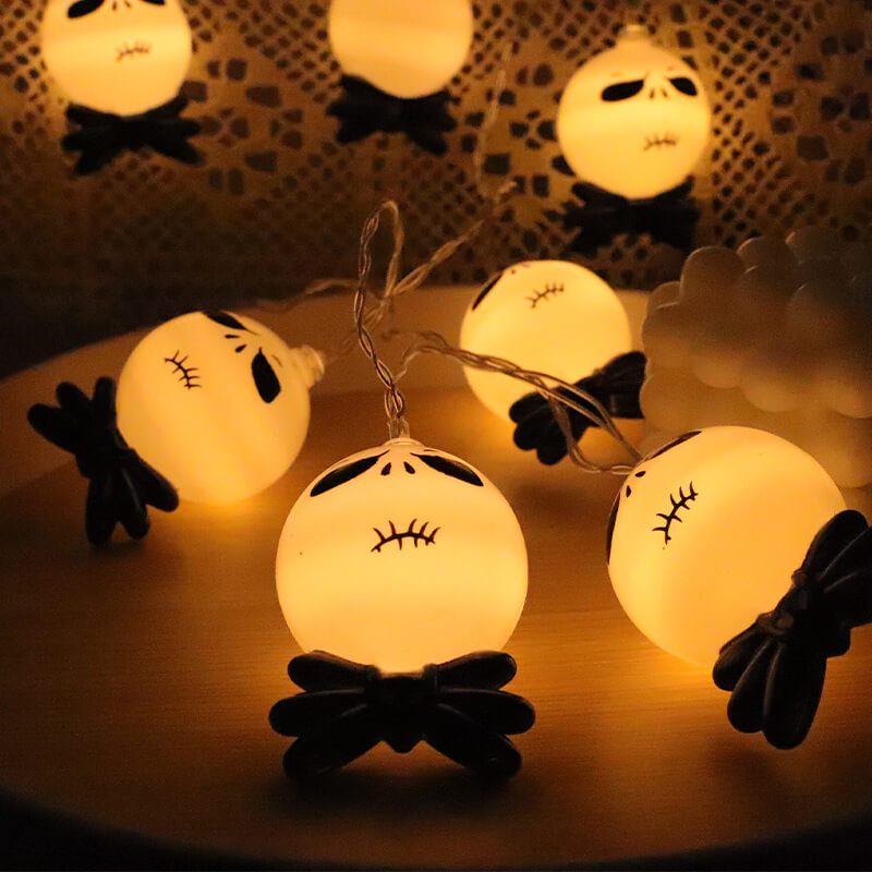 Lit string light heads lying on a round wooden table, the front one standing upright on its black bow tie