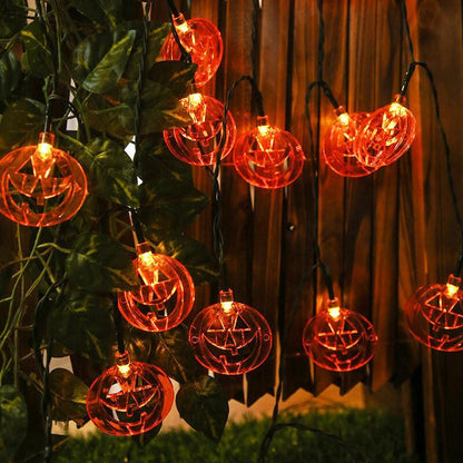 Pumpkin face string lights hung down a wooden fence through ivy, each flat orange pumpkin glowing with its face cut through