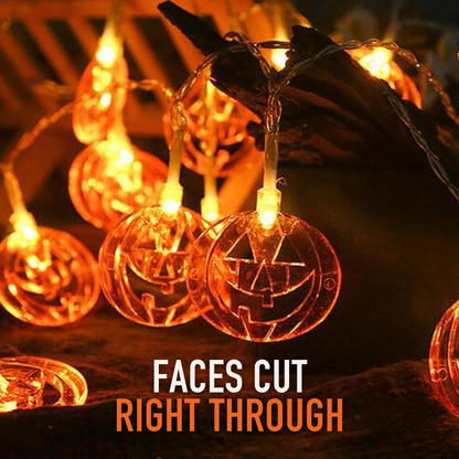 Close view of lit pumpkin string lights over driftwood, with the words Faces cut right through
