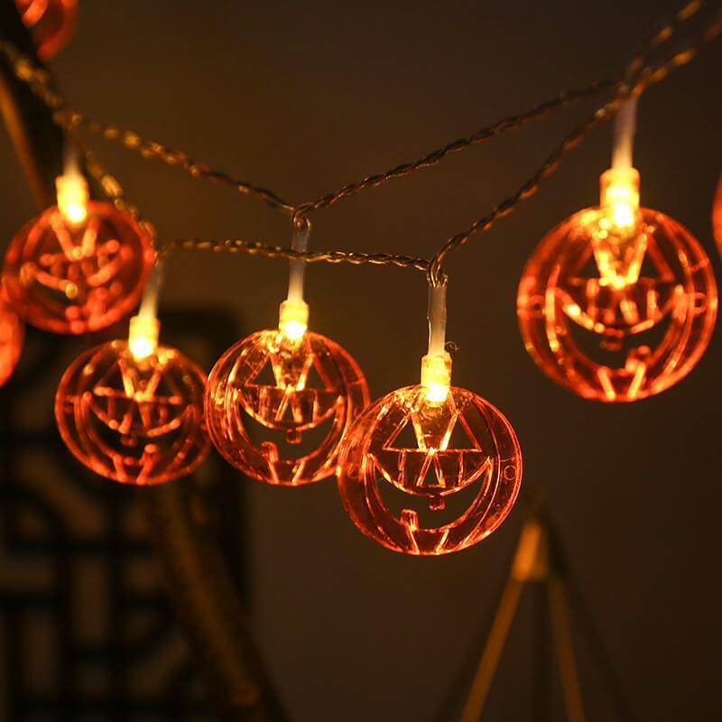Pumpkin string lights on clear wire swagged across a dark wall, the triangle eyes and grin glowing orange