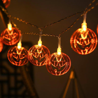 Pumpkin string lights on clear wire swagged across a dark wall, the triangle eyes and grin glowing orange