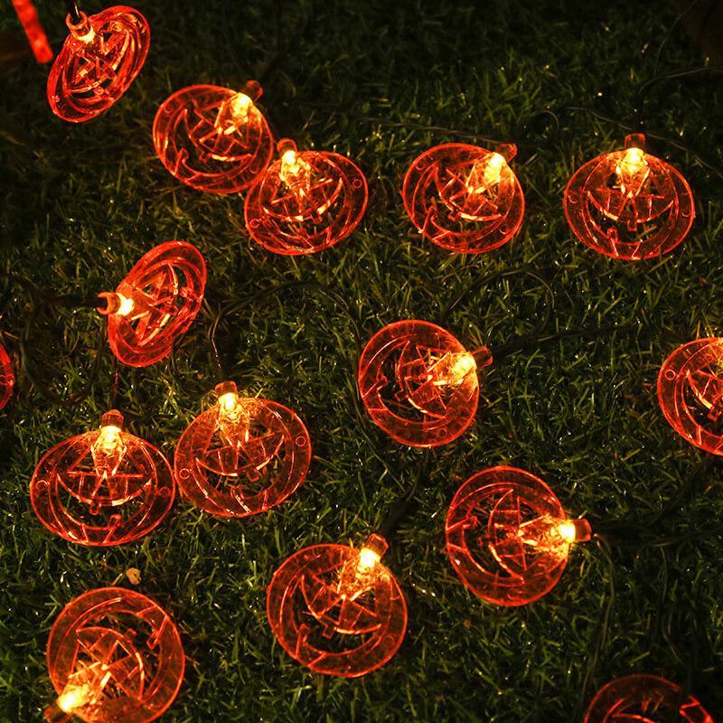 Lit pumpkin face string lights on dark green wire lying on a lawn at night