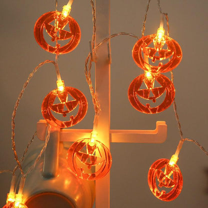 Pumpkin string lights draped over a white display stand, the flat faces glowing against a grey wall