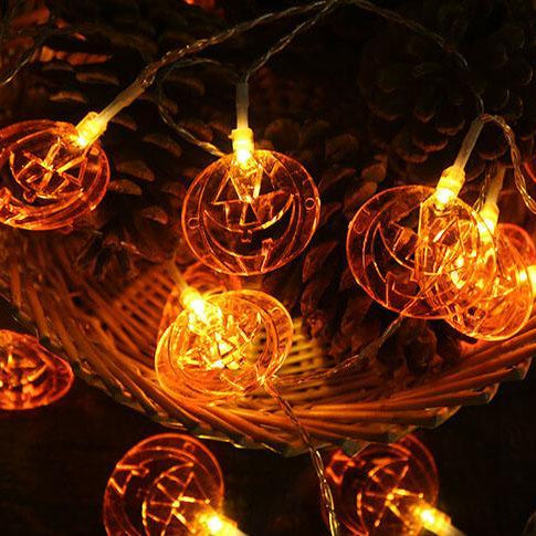 Lit pumpkin string lights heaped in a wicker basket with pine cones
