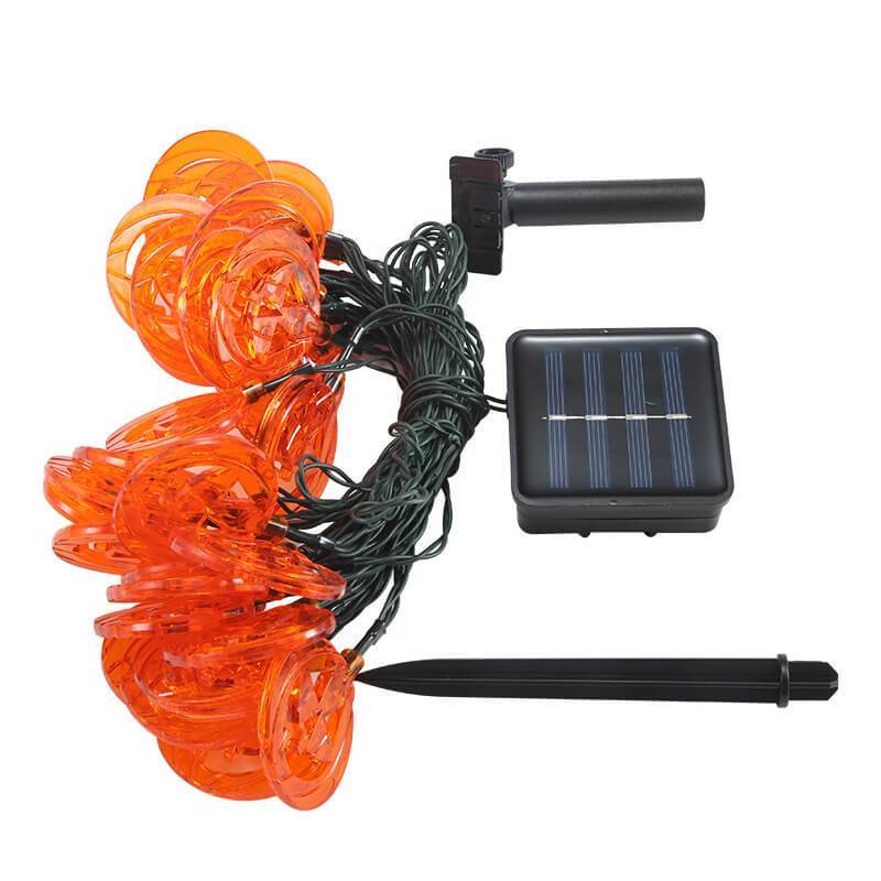 Solar pumpkin string lights unlit on white, with the coiled dark green wire, square solar panel, mount and ground stake