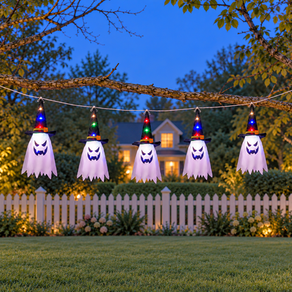 String of five witch hat ghost lights hanging from a tree branch in a front yard at dusk