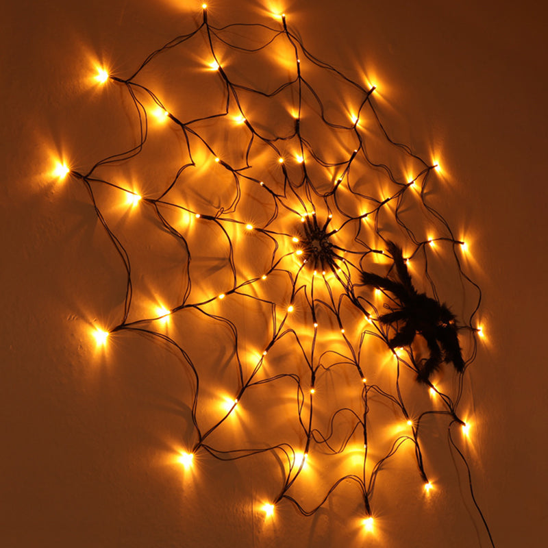 Amber lit spider web light on a wall with a plush spider on it