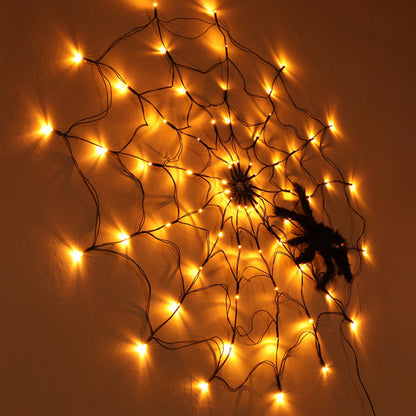 Amber lit spider web light on a wall with a plush spider on it