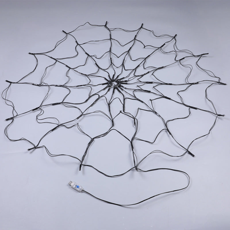 Unlit black wire spider web light laid flat on a grey floor with its USB plug