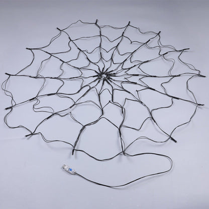 Unlit black wire spider web light laid flat on a grey floor with its USB plug