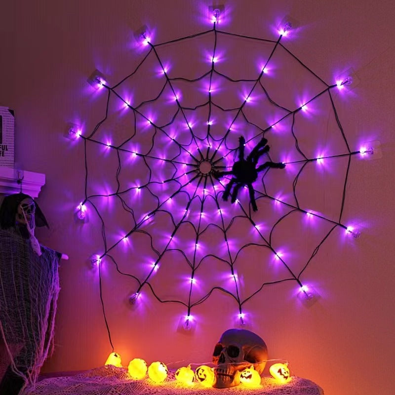 Purple lit spider web light on a wall above a skull and pumpkin lights