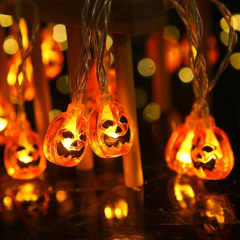 Two lit orange jack-o'-lantern bulbs on a clear wire, close up, glowing under a wooden stool