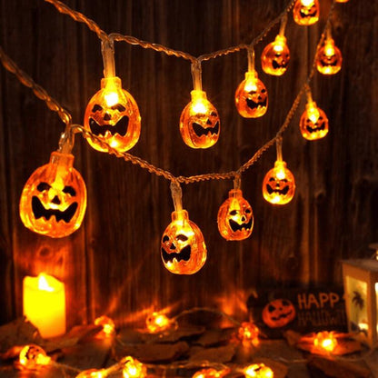 Lit orange jack-o'-lantern string lights on a clear wire swagged across a dark wooden plank wall, with candles below