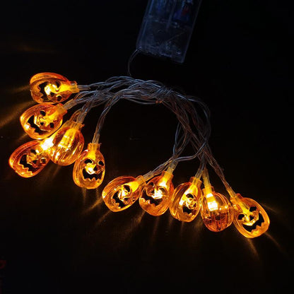 Ten lit orange jack-o'-lantern bulbs laid around a clear battery box on a black surface