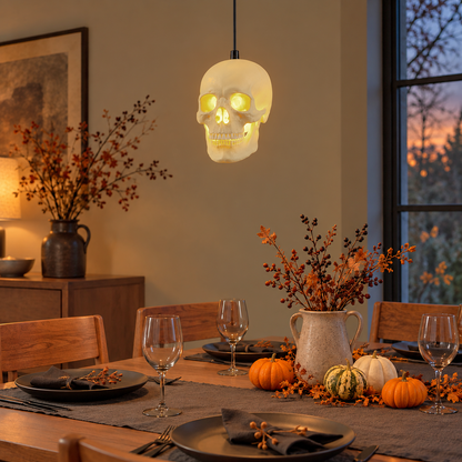 Skull pendant light glowing over a Halloween dinner table set with small pumpkins