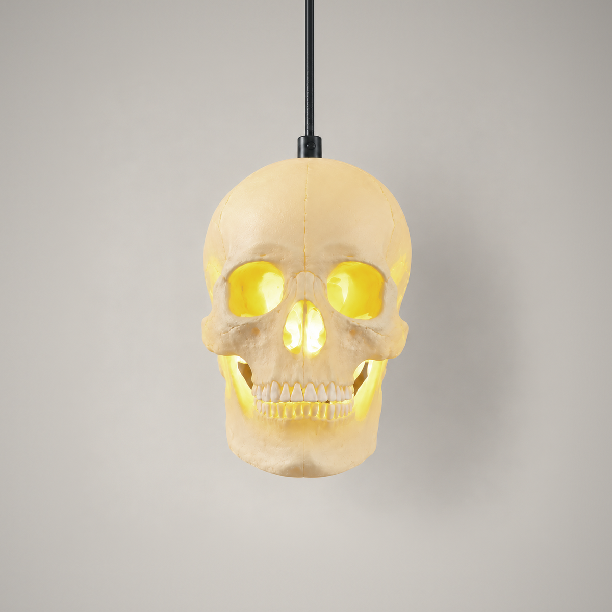 Skull pendant light switched on, face on, the eye sockets, nose and teeth glowing, on a grey background