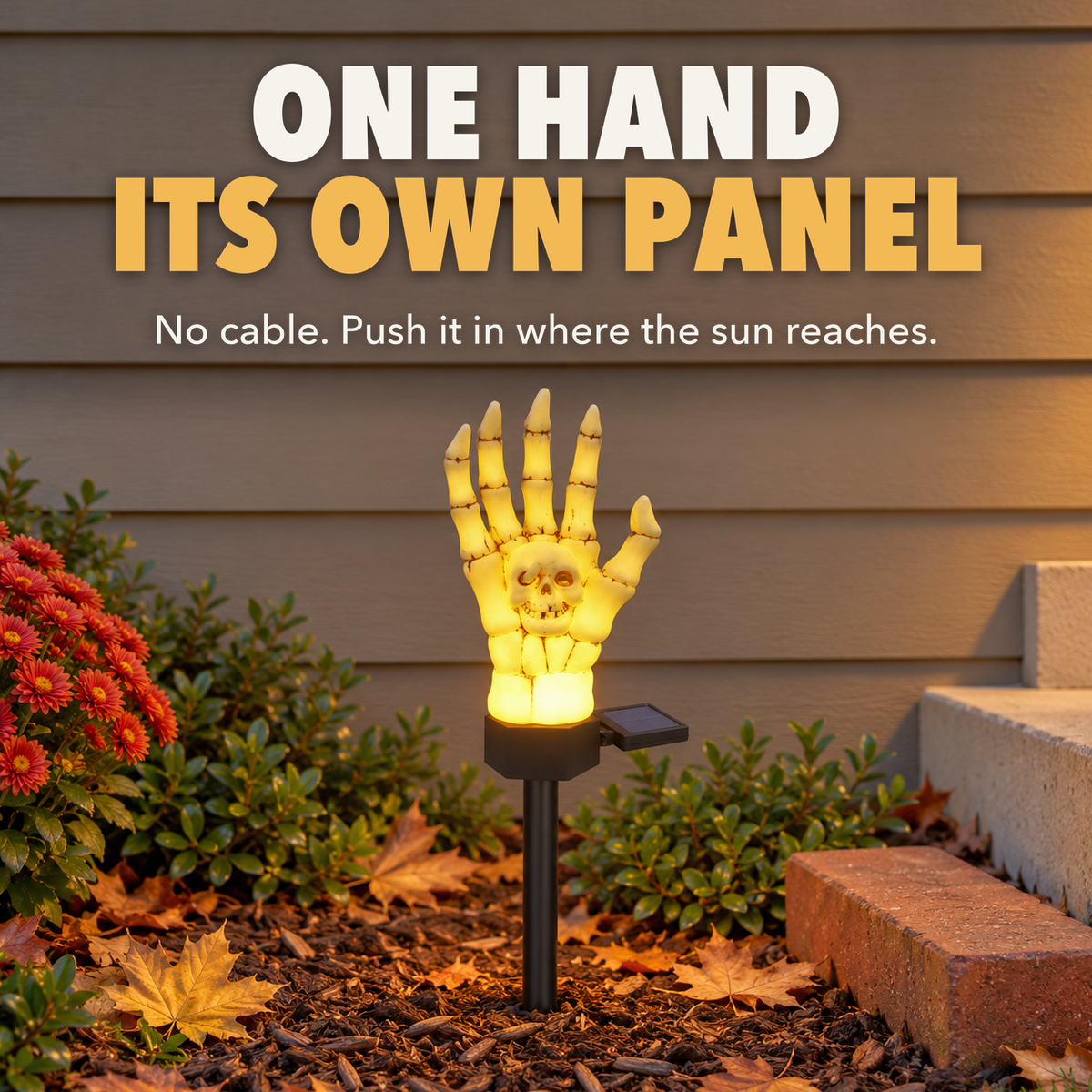 A single glowing skeleton hand stake light in a flowerbed against a house wall, with the words One hand, its own panel