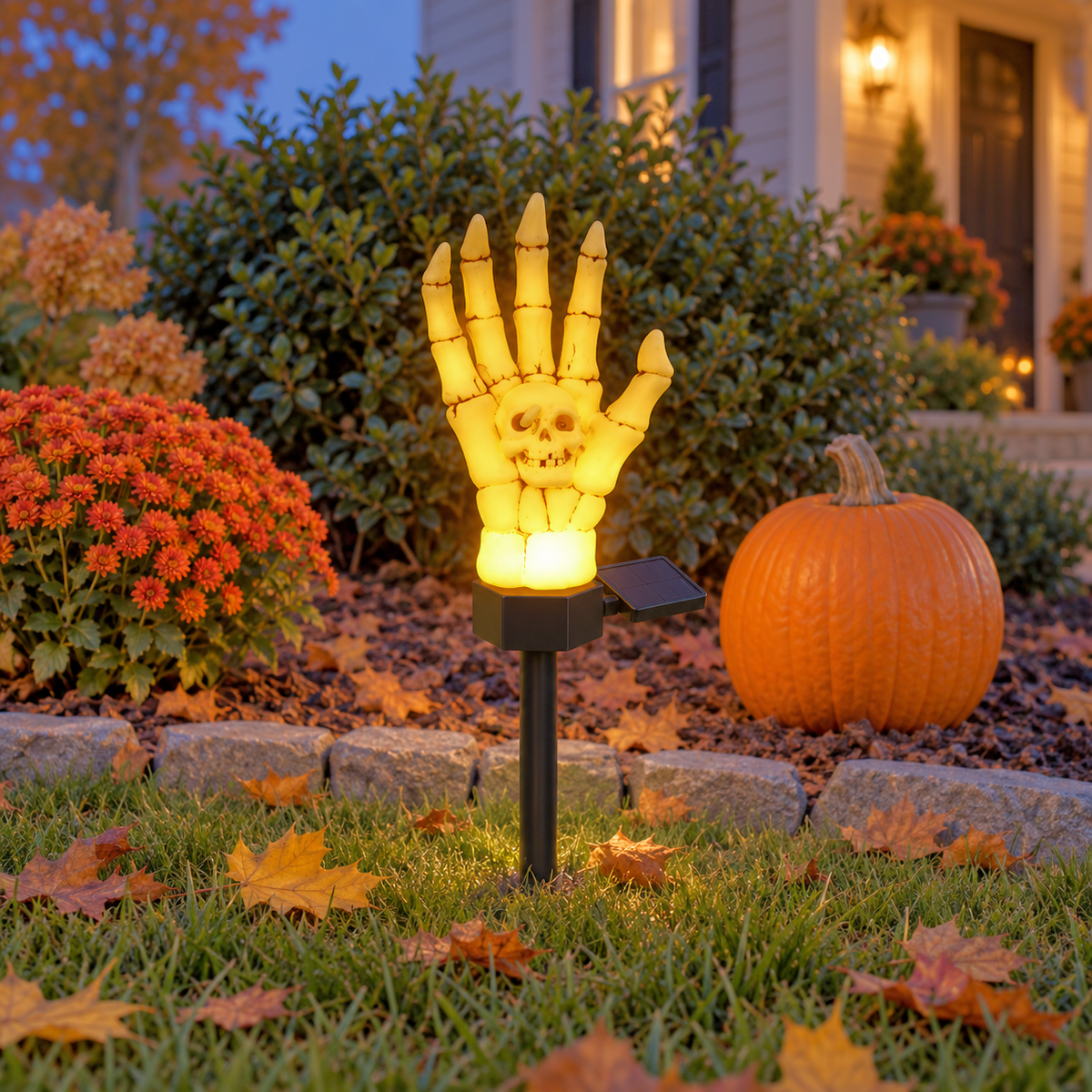 Single skeleton hand stake light glowing warm at the corner of a lawn at dusk beside a small pumpkin