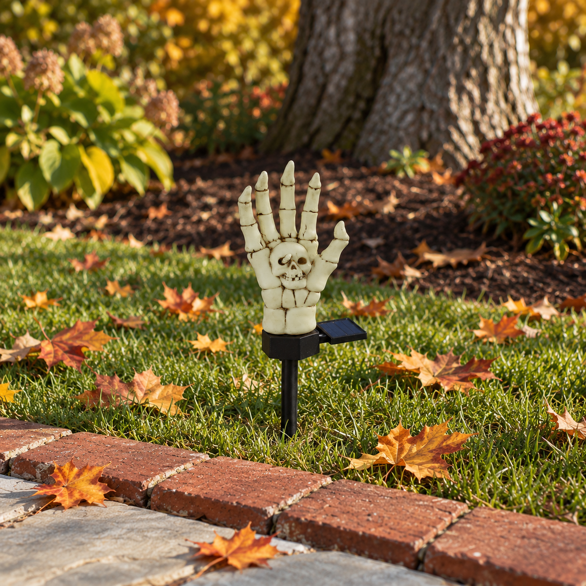 Single bone-colored skeleton hand stake light switched off in the grass beside a brick path edging on a sunny afternoon