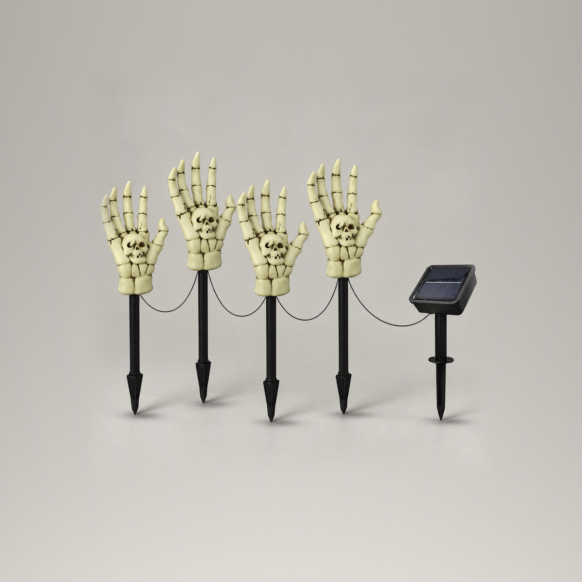 Set of four skeleton hand stake lights with their connecting cable and separate solar panel stake on a plain gray background