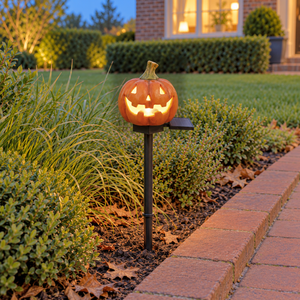 Classic pumpkin stake light glowing through its carved face at dusk in a border beside a brick path