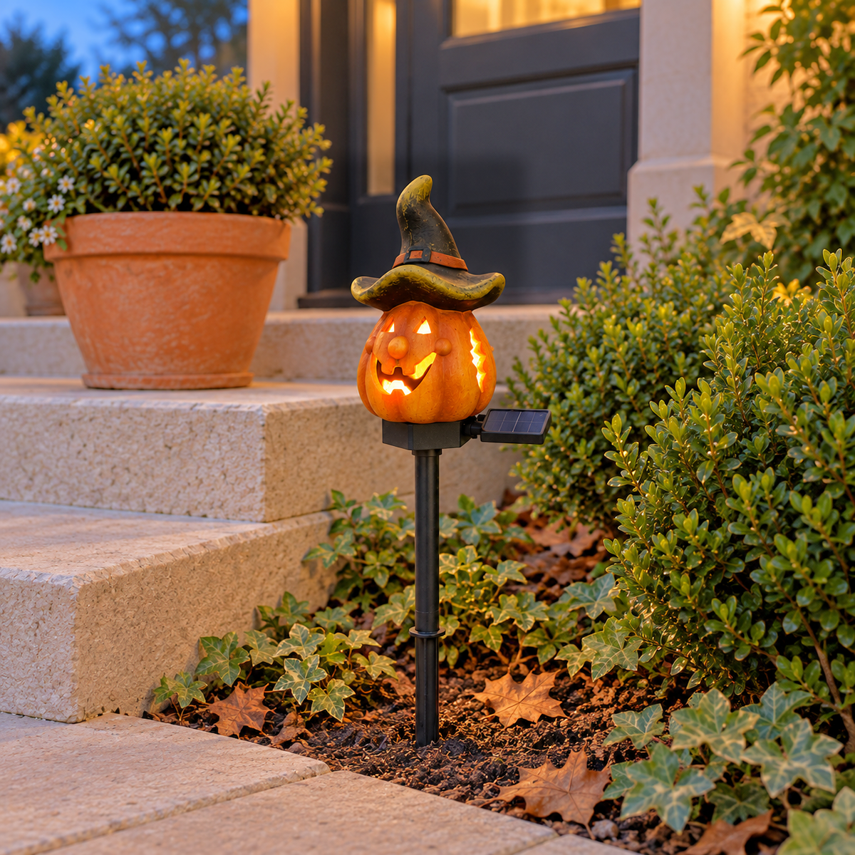 Witch Hat pumpkin stake light glowing through its eyes and grin beside stone front steps at dusk