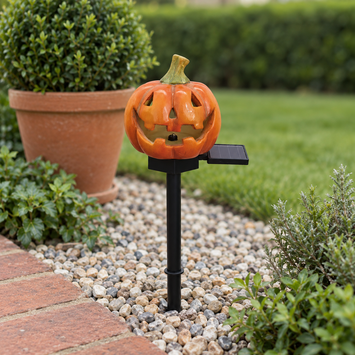 Classic pumpkin stake light switched off in a gravel border beside a brick path and a terracotta pot