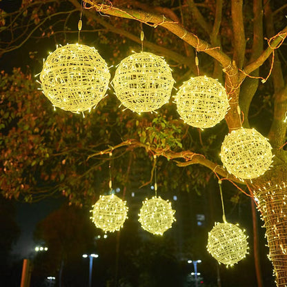 Warm white LED ball lights in two sizes hanging on thin leads from the limb of a tree at night