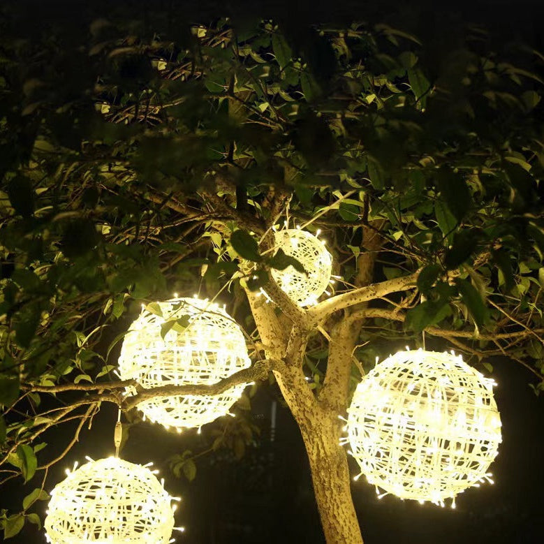 Four warm white LED ball lights in two sizes hanging among the branches of a tree at night