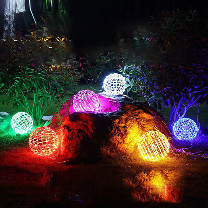 LED ball lights in several colors resting on a garden rock and lawn at night