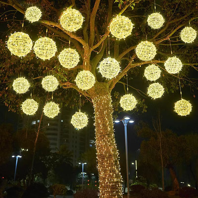 Many warm white LED ball lights hanging throughout a large tree in a park at night
