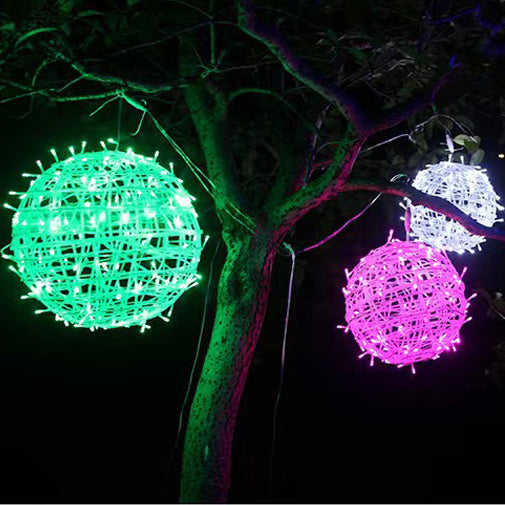 Green, pink and white LED ball lights hanging from the branches of a tree at night