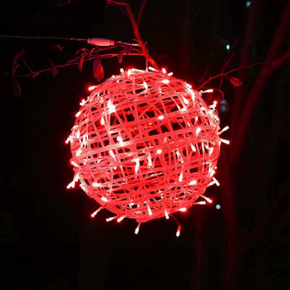 A red LED ball light hanging below a branch at night, its lead running along the branch