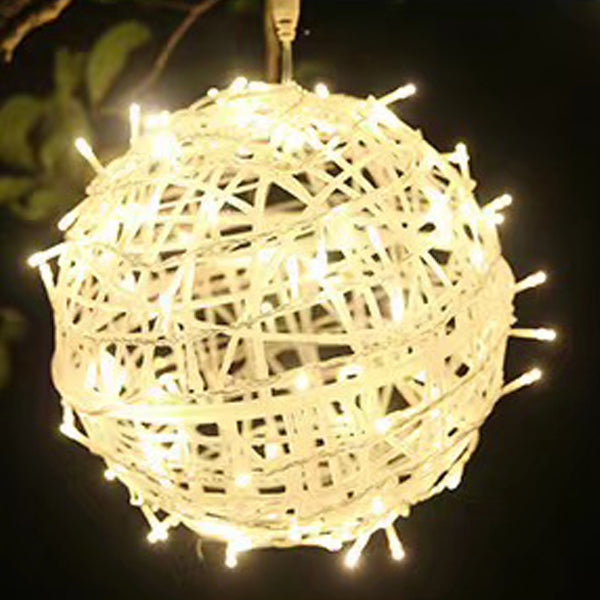 A warm white LED ball light glowing close up among leaves
