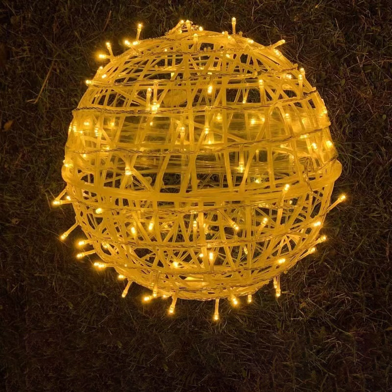 A yellow LED ball light with a yellow woven housing resting on grass at night
