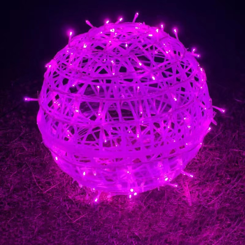 A pink LED ball light resting on grass at night