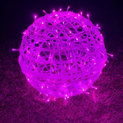 A pink LED ball light resting on grass at night
