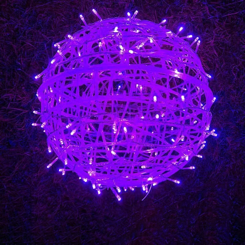A purple LED ball light resting on grass at night