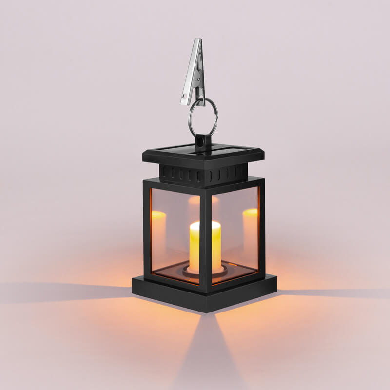 Solar candle lantern glowing warm amber through four clear panels, with a metal hanging clip on top