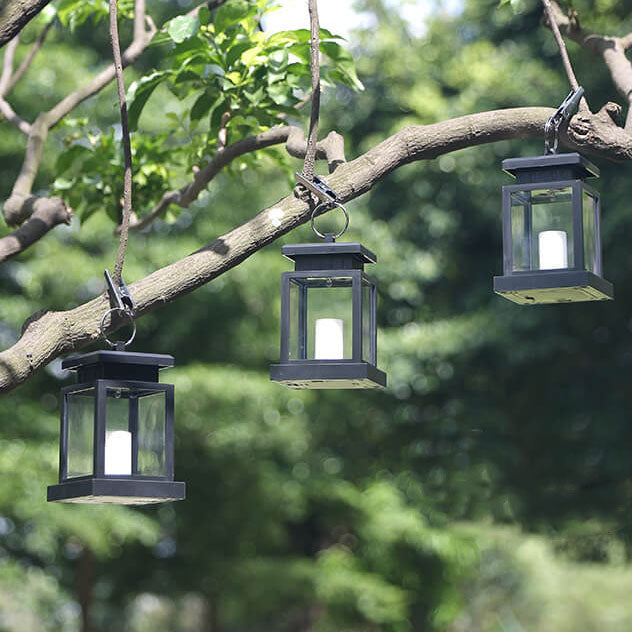 Three black solar candle lanterns clipped under a tree branch in daylight