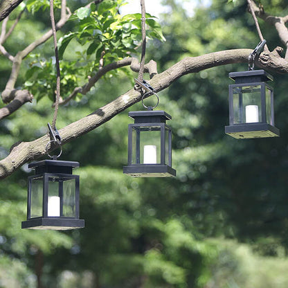 Three black solar candle lanterns clipped under a tree branch in daylight