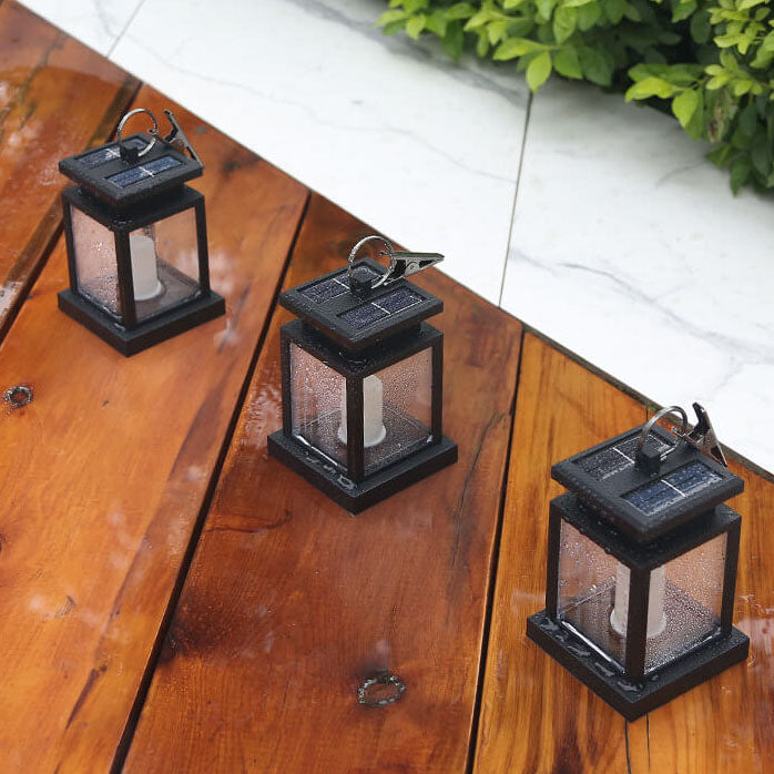 Three solar candle lanterns standing on wet wooden deck boards beside a marble step, rain beaded on their panels