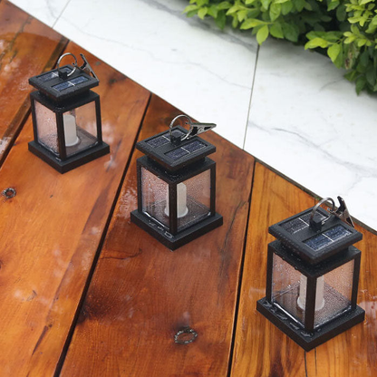 Three solar candle lanterns standing on wet wooden deck boards beside a marble step, rain beaded on their panels