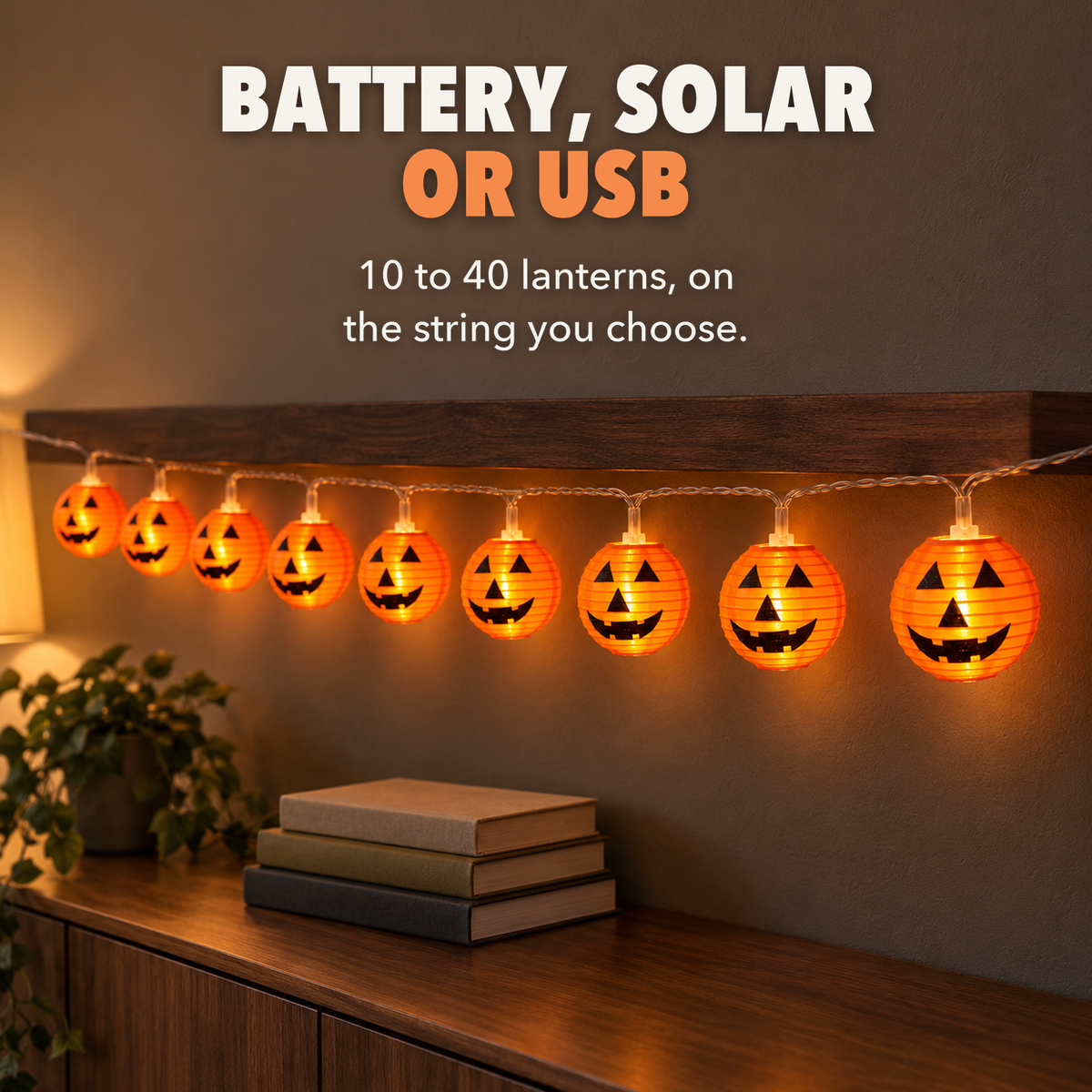 Lit orange lantern string lights with jack-o'-lantern faces under a walnut shelf indoors, with the words Battery, solar or USB