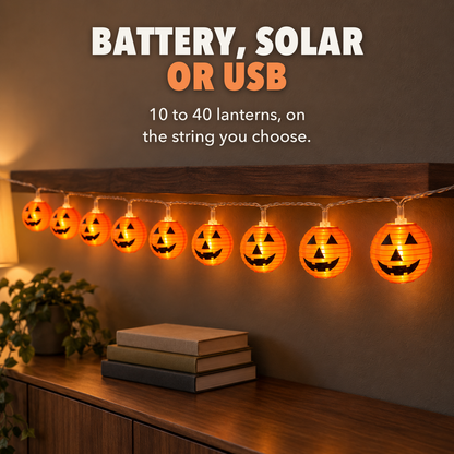 Lit orange lantern string lights with jack-o'-lantern faces under a walnut shelf indoors, with the words Battery, solar or USB